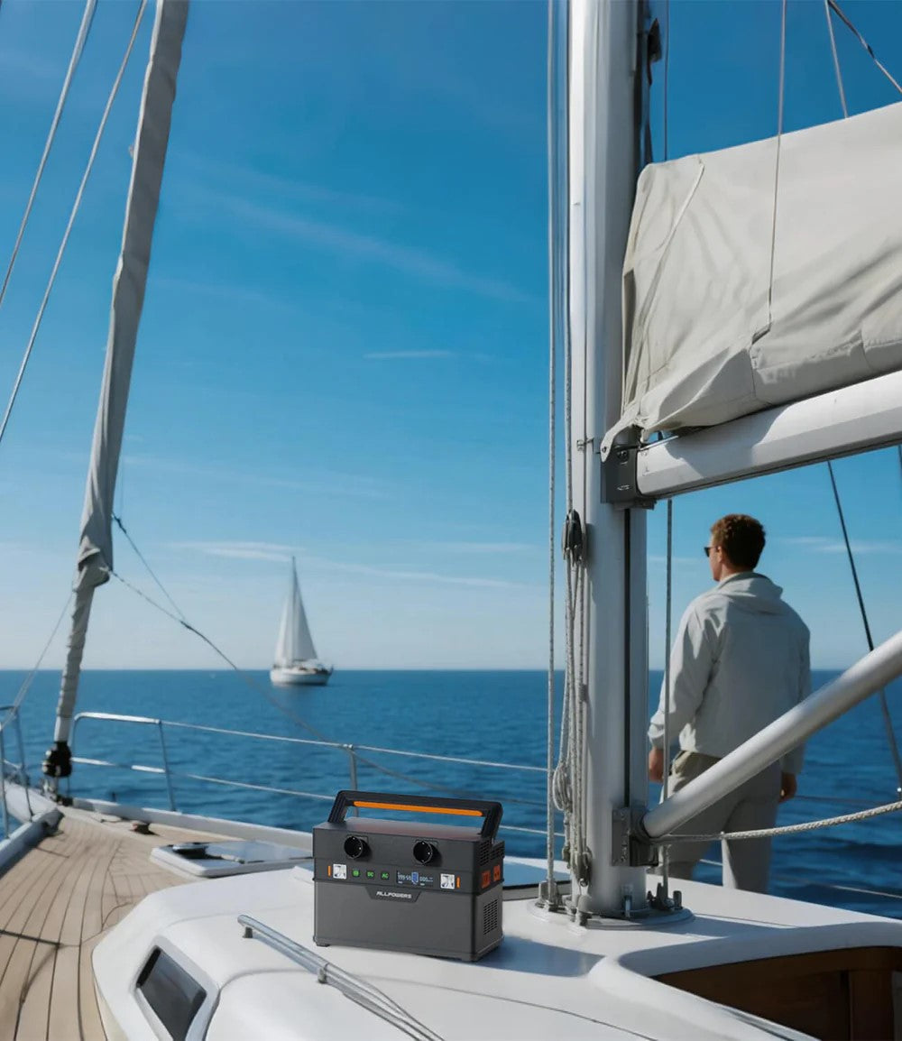 Um homem de pé no convés de um iate moderno sob o sol, observando um barco a vela, com uma estação de energia portátil destacada na superfície do convés.