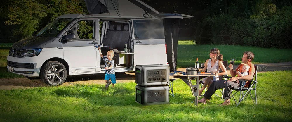 Família aproveitando acampamento ao lado de uma van camper, com duas estações de energia portáteis ALLPOWERS empilhadas na grama sob luz do dia
